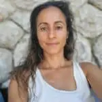 Femme souriante devant un mur en pierre.